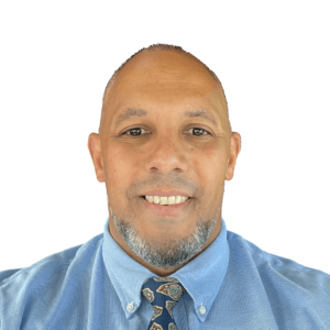 Headshot of Machael Anderson, a Brown man with dark eyes, little hair, and a well-groomed beard that's greying. He's wearing a blue suit and tie.