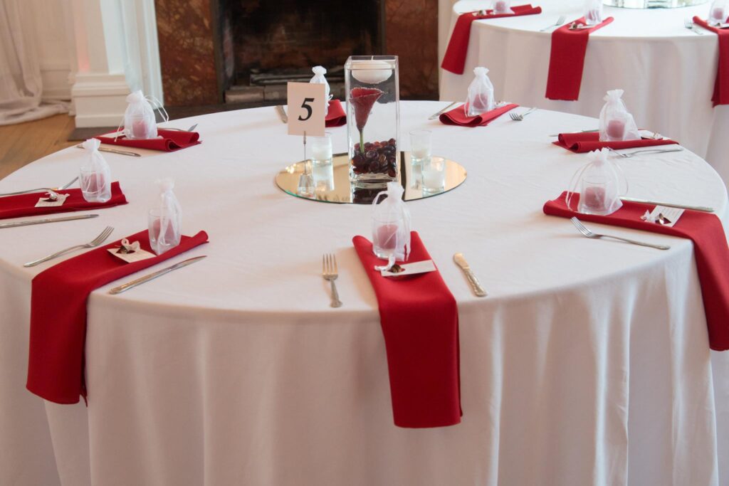 A round table dressed with a white table cloth and red napkins, supplied by Mosaic for a wedding reception.